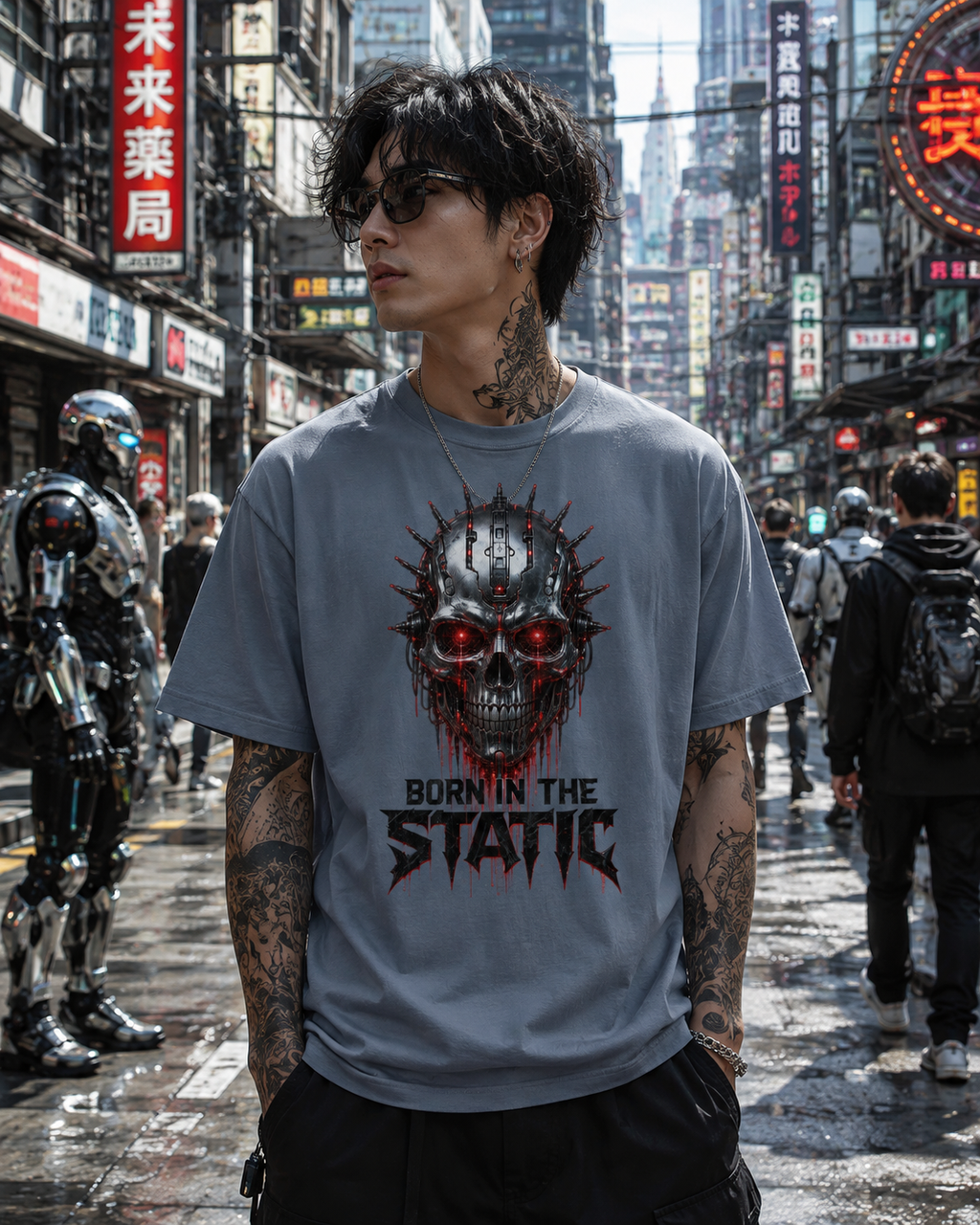 A man wearing a light gray graphic t-shirt with a red and black skull design and the text 'BORN IN THE STATIC' stands on a wet, busy city street with neon signs and robotic figures in the background.