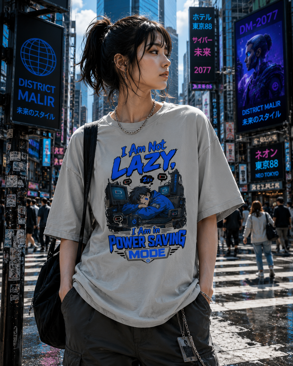 A woman wearing an oversized light gray graphic T-shirt with blue and black text reading 'I Am Not Lazy, I Am Power Saving Mode' stands on a busy city street with neon signs and pedestrians in the background.
