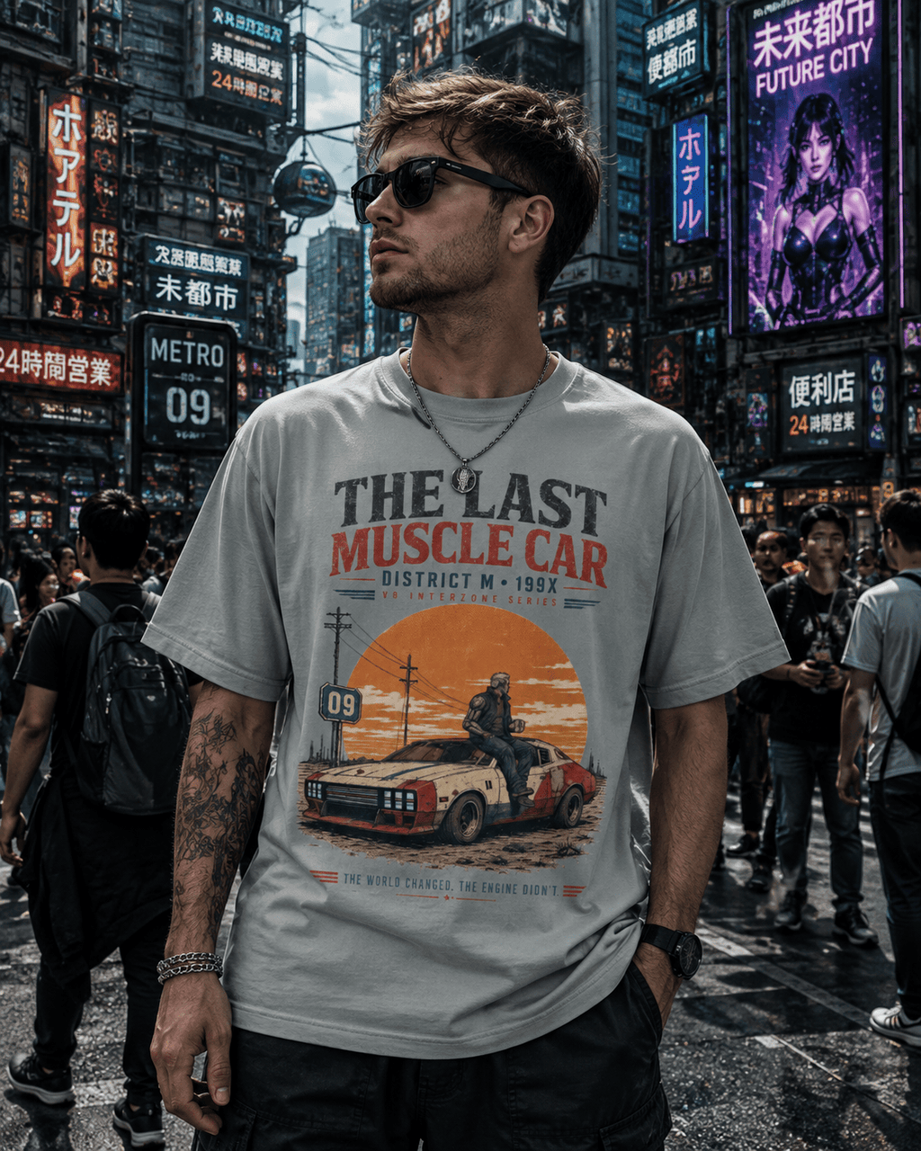 A man wearing a light gray graphic t-shirt with a red and orange 'The Last Muscle Car' print, standing in a busy neon-lit city street.